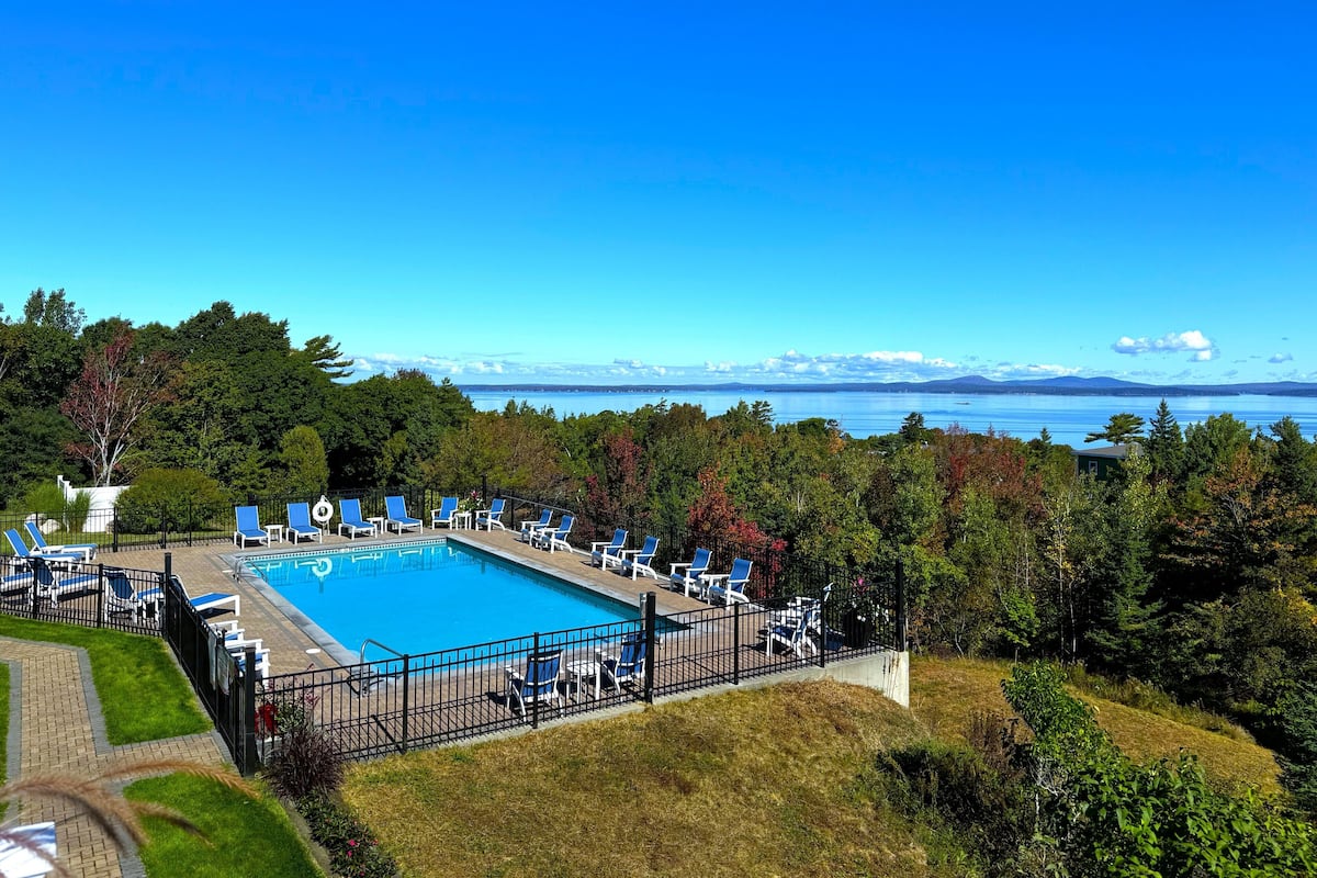Piscina com espreguiçadeiras e vista para um lago e montanhas.