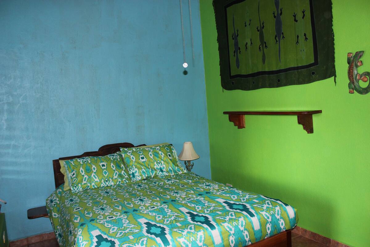 A room with a bed, a wall hanging, and a shelf.