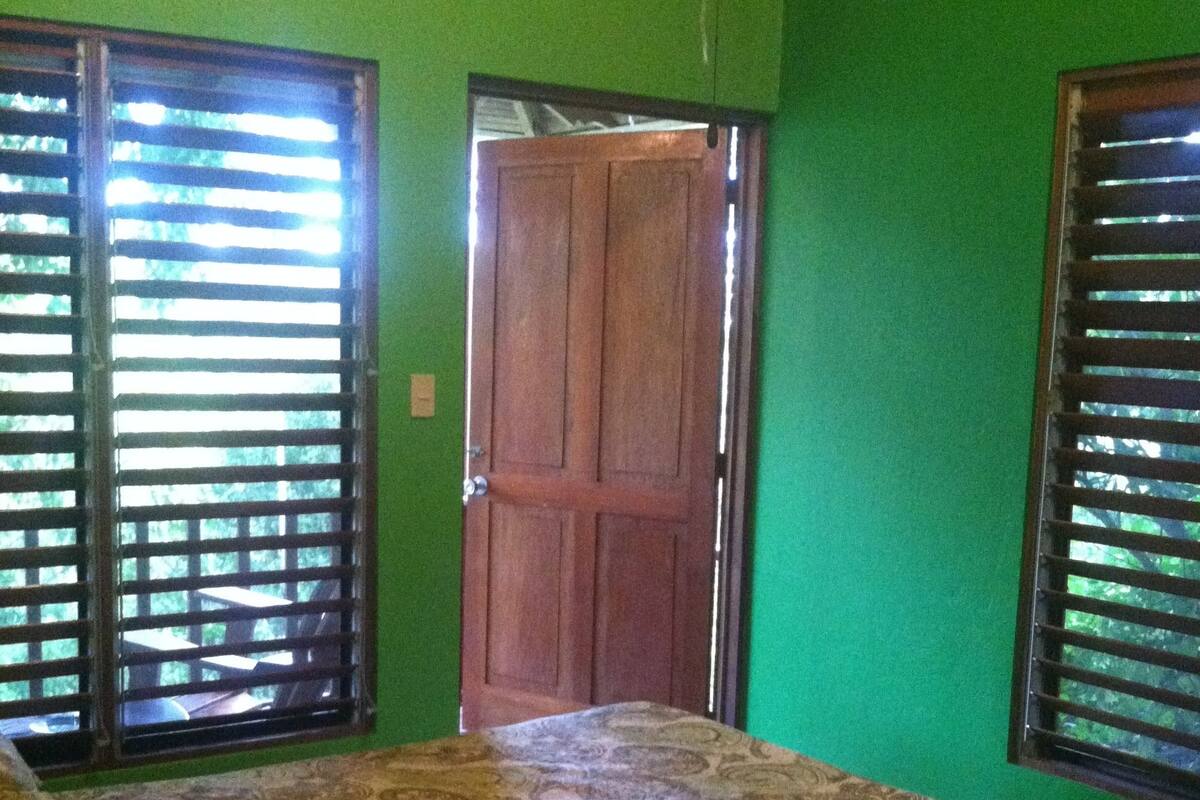 A room with green walls, a wooden door, and a bed with a patterned bedspread.
