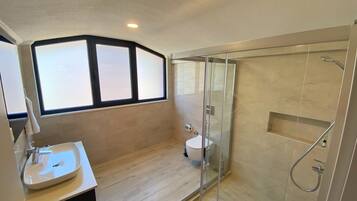 Un baño moderno con ducha envuelta en vidrio, un lavabo blanco y una ventana que permite la entrada de luz natural.