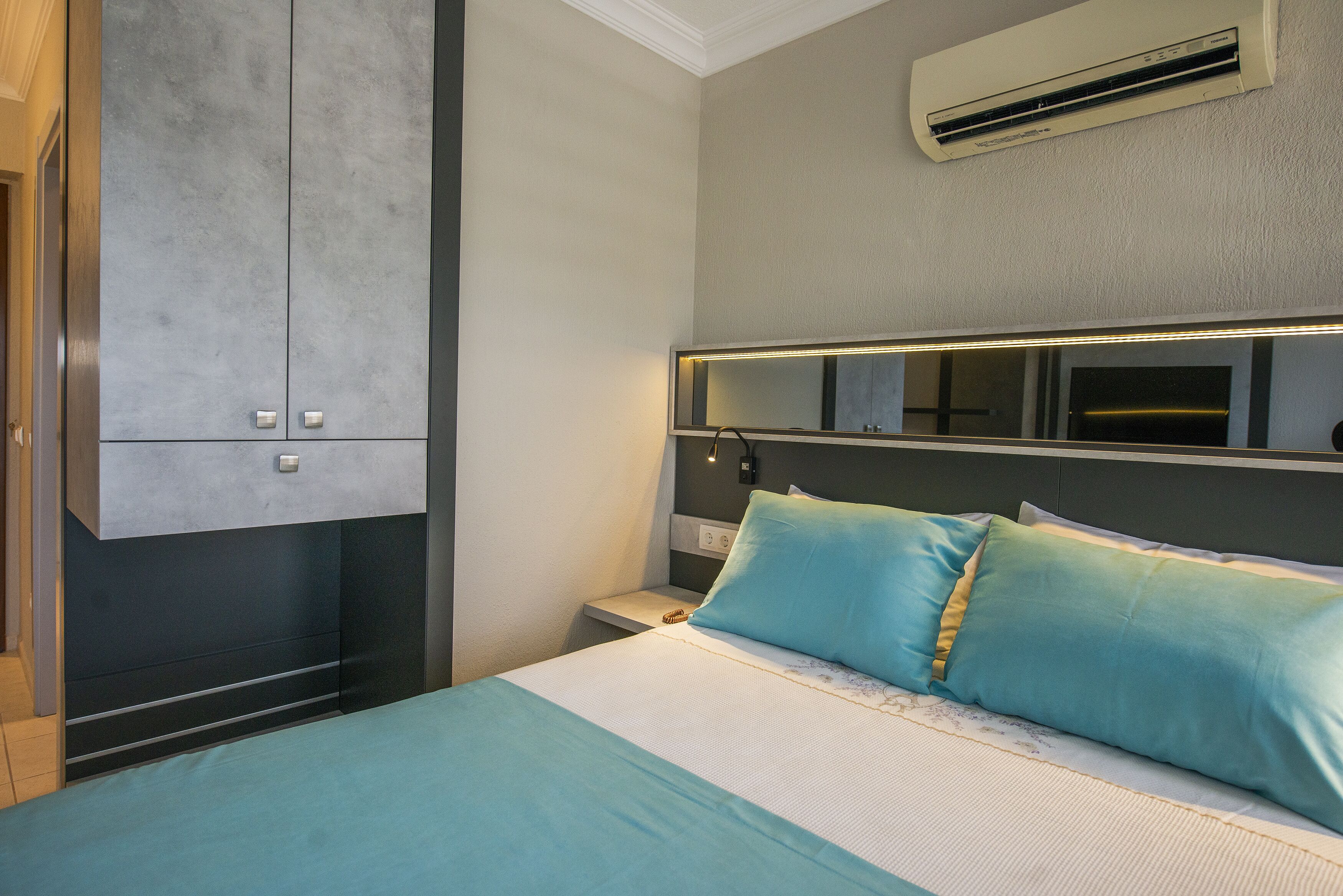 A bedroom with a bed, a nightstand, a wall-mounted air conditioner, and a wardrobe.