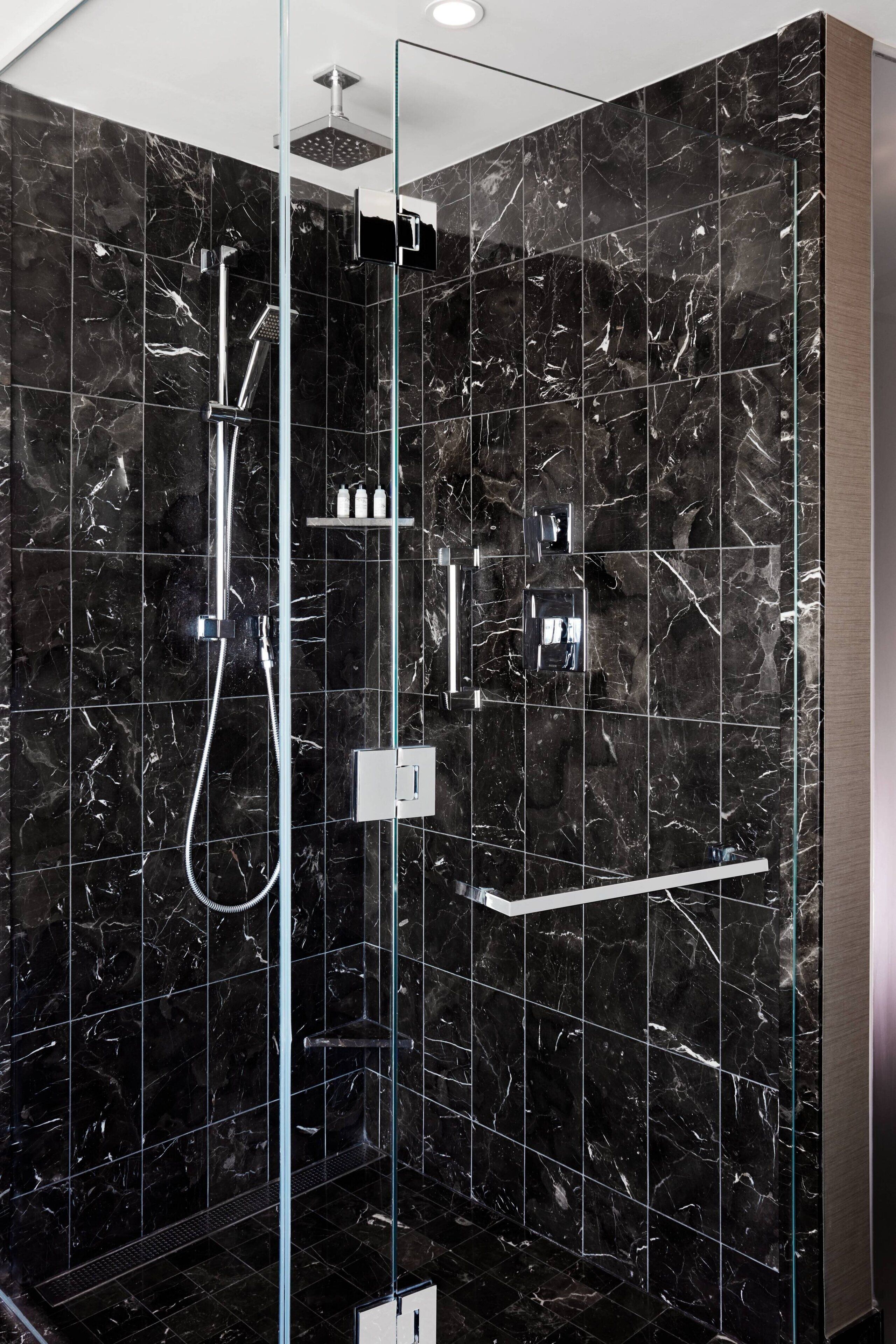A modern shower with a glass enclosure, a handheld showerhead, and a wall-mounted control panel.
