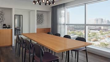 Un comedor moderno con una larga mesa de madera, sillas oscuras y vistas a la ciudad a través de amplios ventanales.