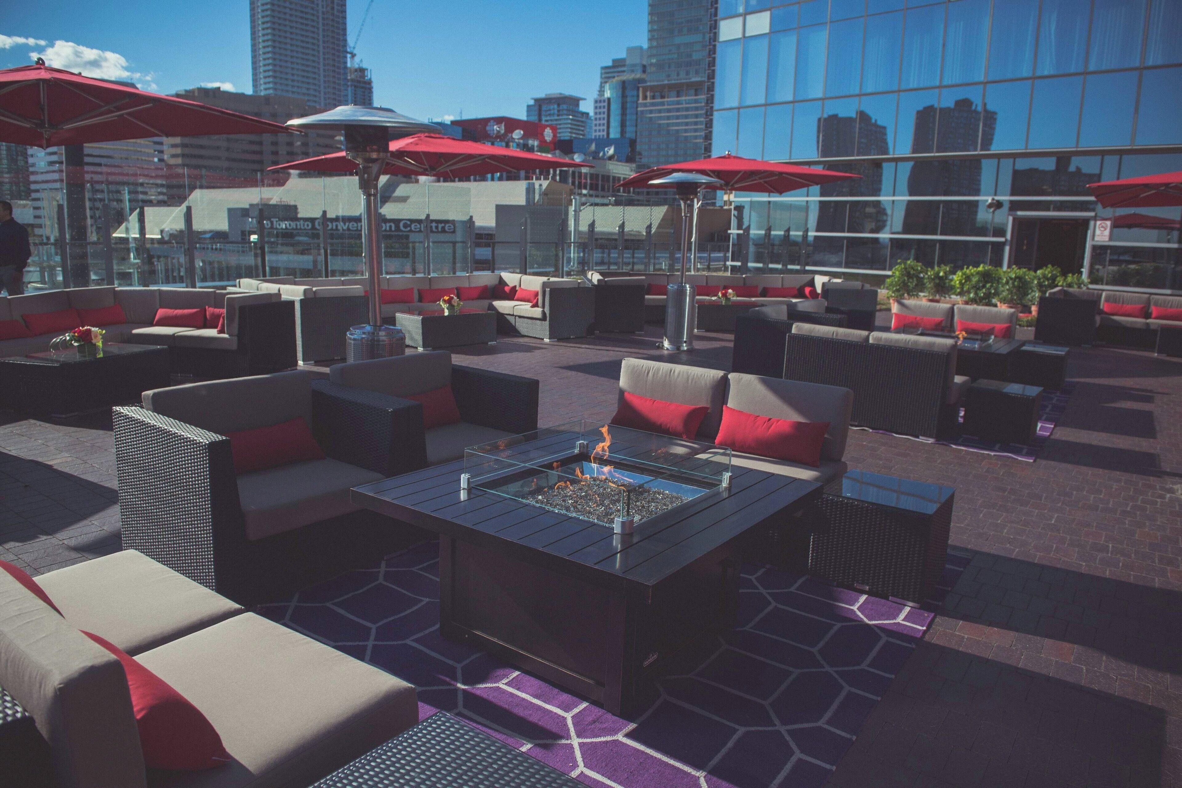 A rooftop lounge with outdoor seating, a fire feature, and red umbrellas.
