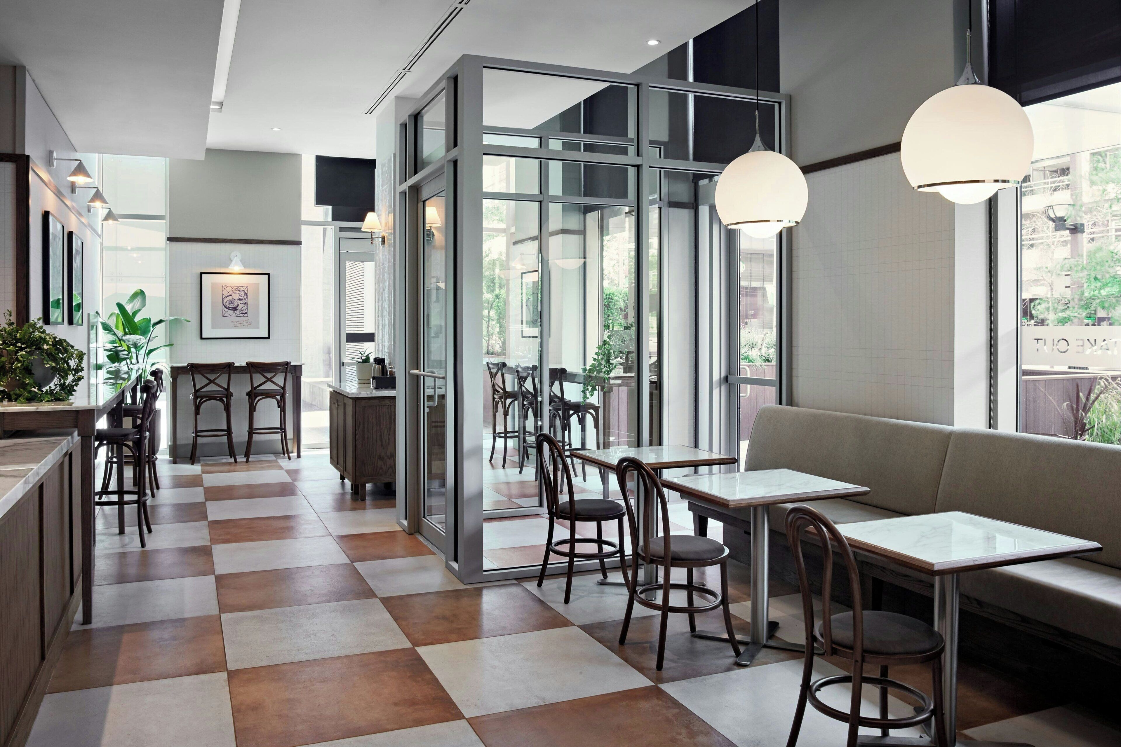 A modern cafe with checkered flooring, glass partitions, and a mix of seating options including tables and a sofa.
