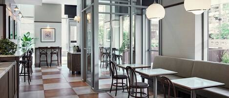 A modern cafe with checkered flooring, glass partitions, and a mix of seating options including tables and a sofa.