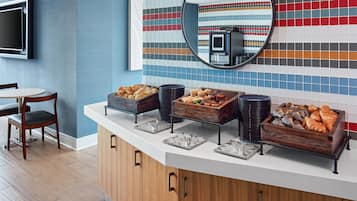 Un bufé de desayuno con diversos alimentos, un televisor montado en la pared y un espejo que refleja la habitación.