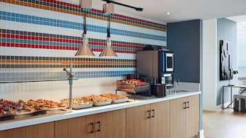 Una cocina moderna con salpicadero de azulejos, un mostrador tipo buffet con diversas opciones de comida y una máquina de café.