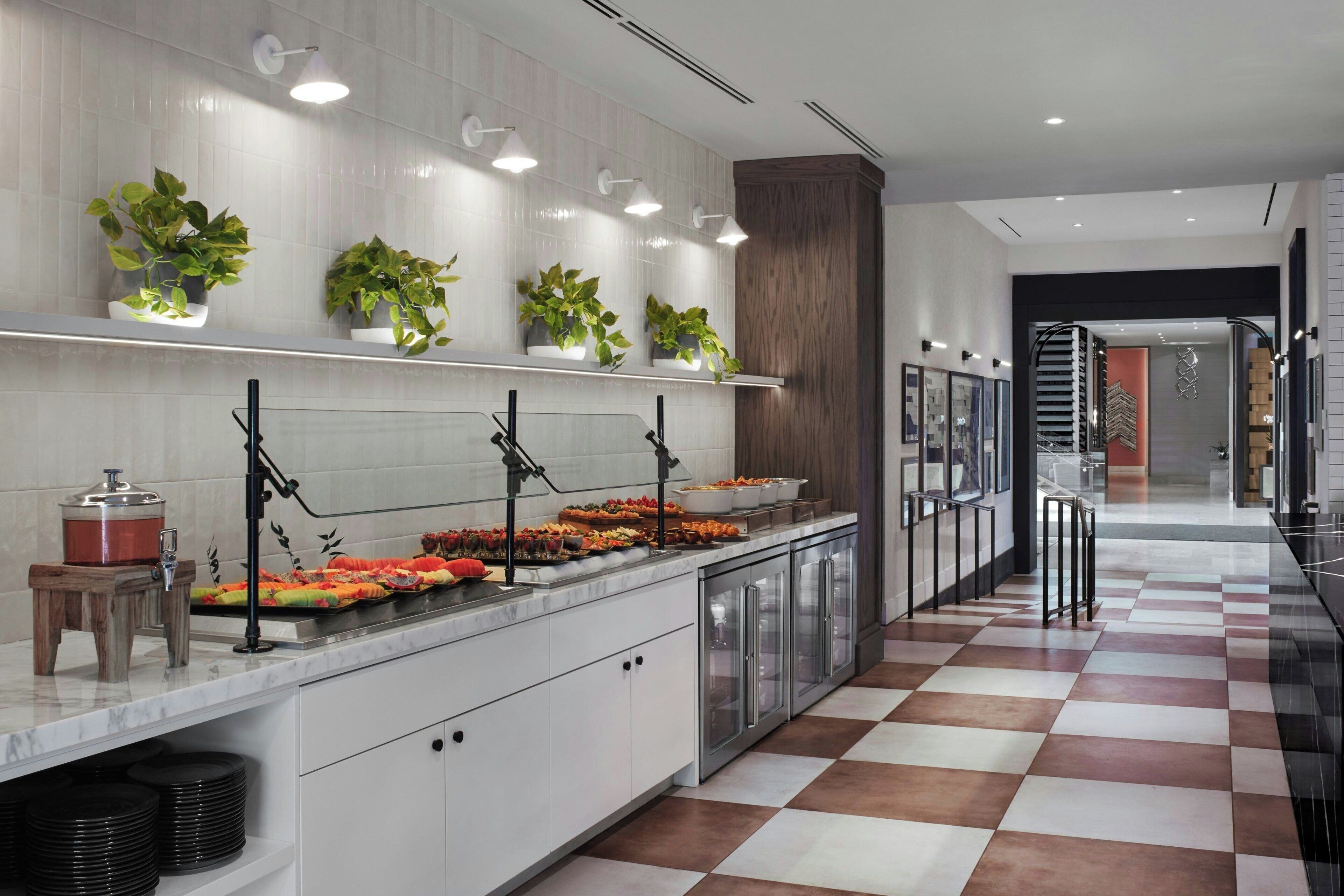 A modern kitchen with a marble countertop, potted plants, and a checkered floor.