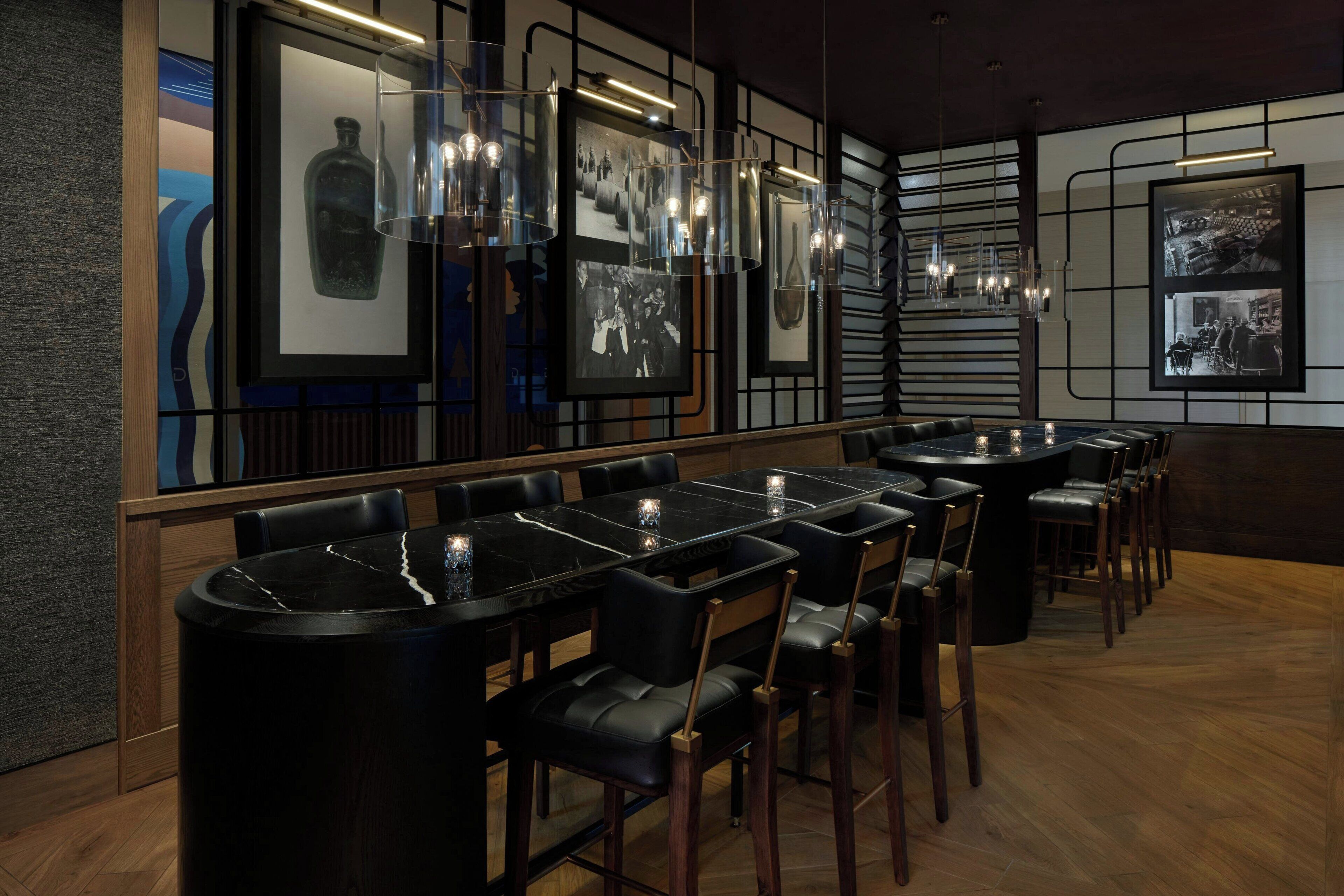 A restaurant with black marble tables and chairs, framed photographs on the walls, and pendant lighting.
