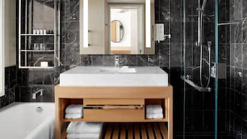 Une salle de bain moderne avec un mur recouvert de carreaux de marbre, un meuble-lavabo en bois et une douche à l’italienne avec des parois en verre.