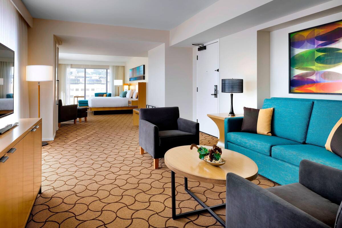 Quarto de hotel com cama, sofá, escrivaninha e mesa de jantar.
