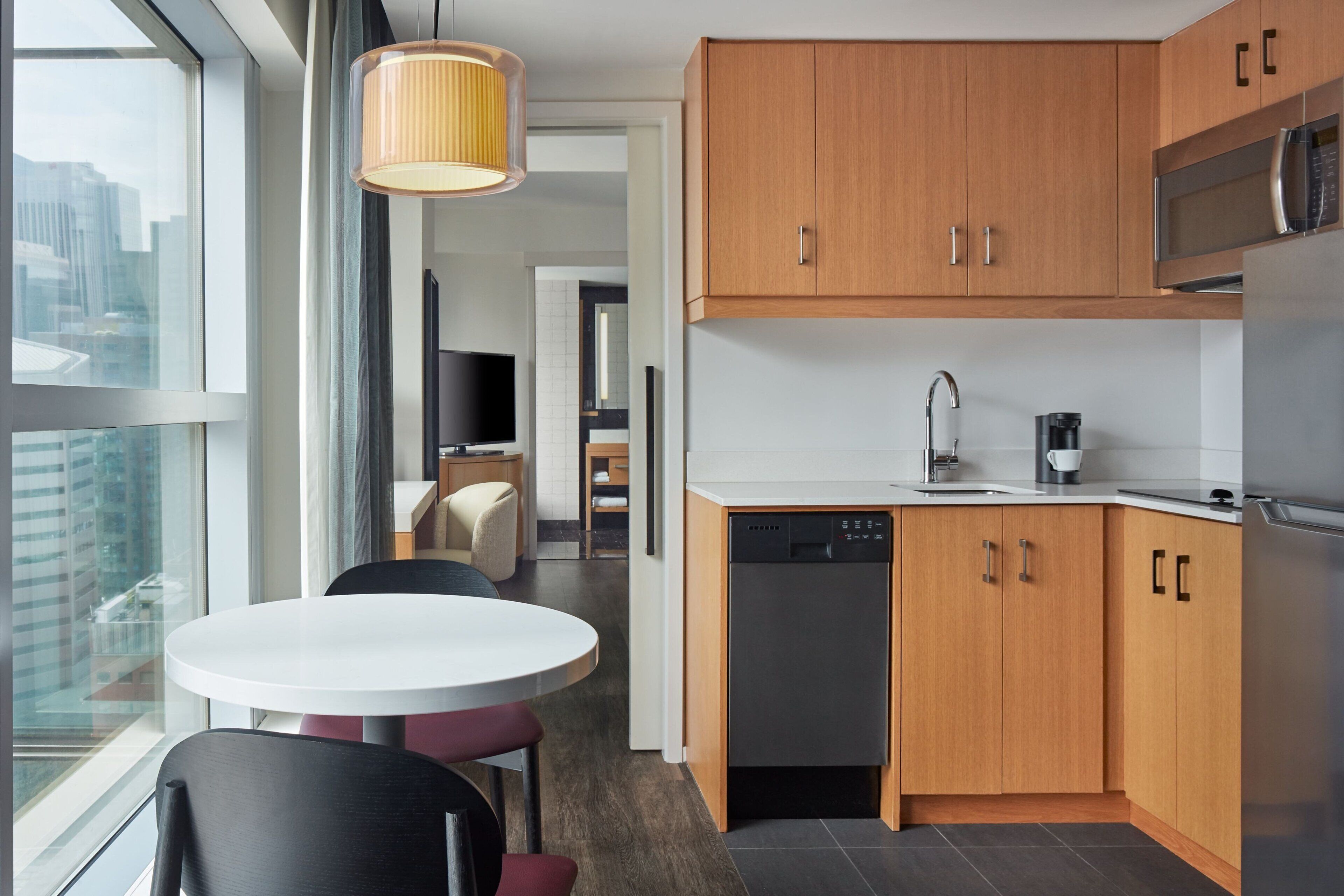 A modern kitchen with wooden cabinets, a dishwasher, and a microwave. There is a dining area with a round table and chairs.