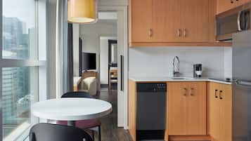 A modern kitchen with wooden cabinets, a dishwasher, and a microwave. There is a dining area with a round table and chairs.