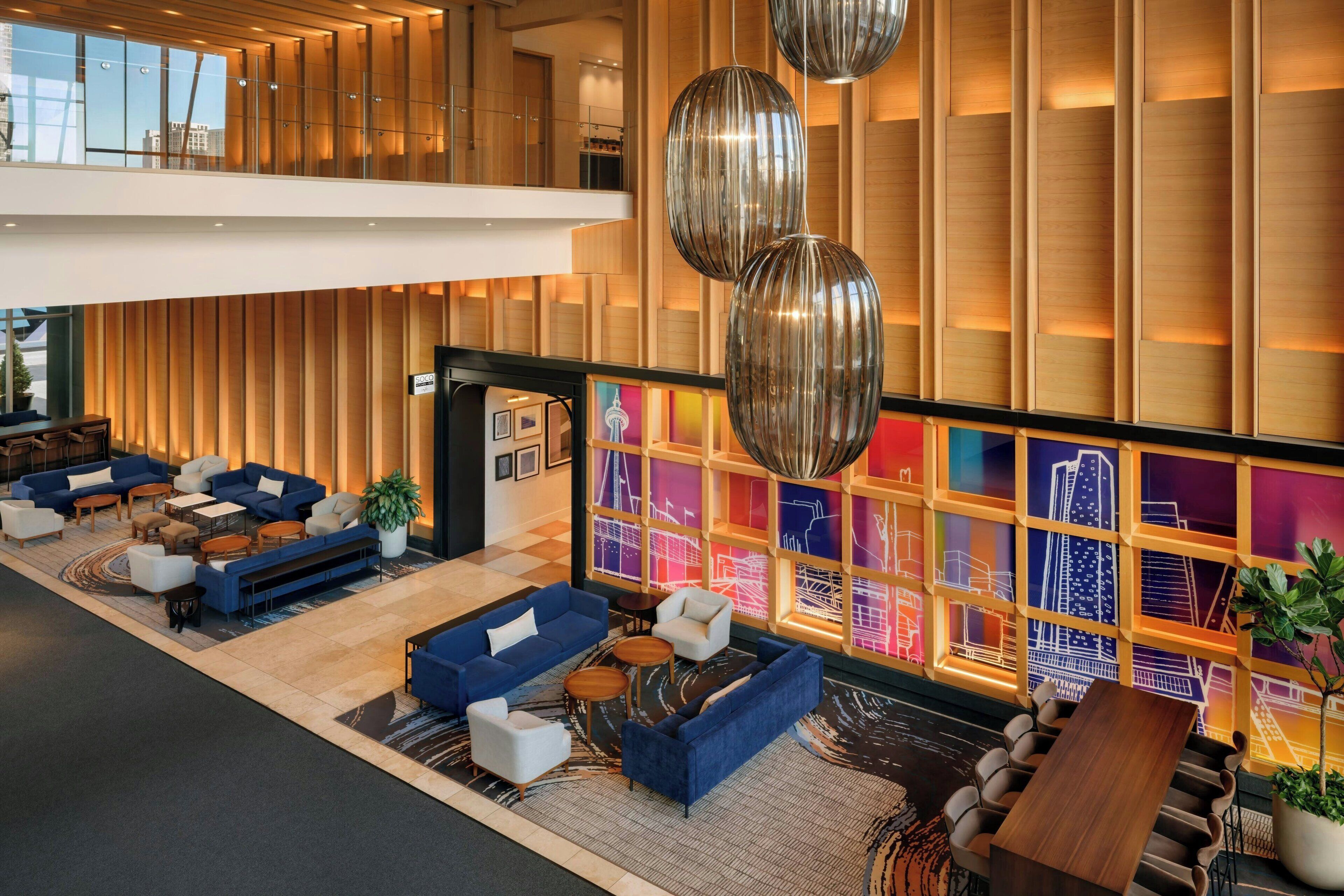 Un hall d’entrée moderne avec des canapés bleus, un comptoir d’accueil en bois et un mur décoré d’une vue colorée sur la ville.
