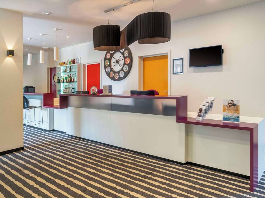 A reception area with a check-in counter, a clock, a television, and a bar with various bottles.