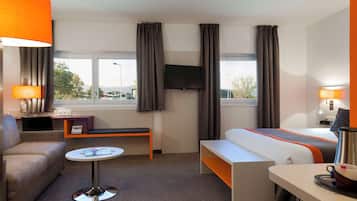 Habitació d'hotel amb llit, sofà, taula petita, televisió i finestra amb cortines.