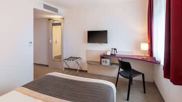 Une chambre d’hôtel avec un lit, un bureau et une chaise, une télévision et une fenêtre avec des rideaux.