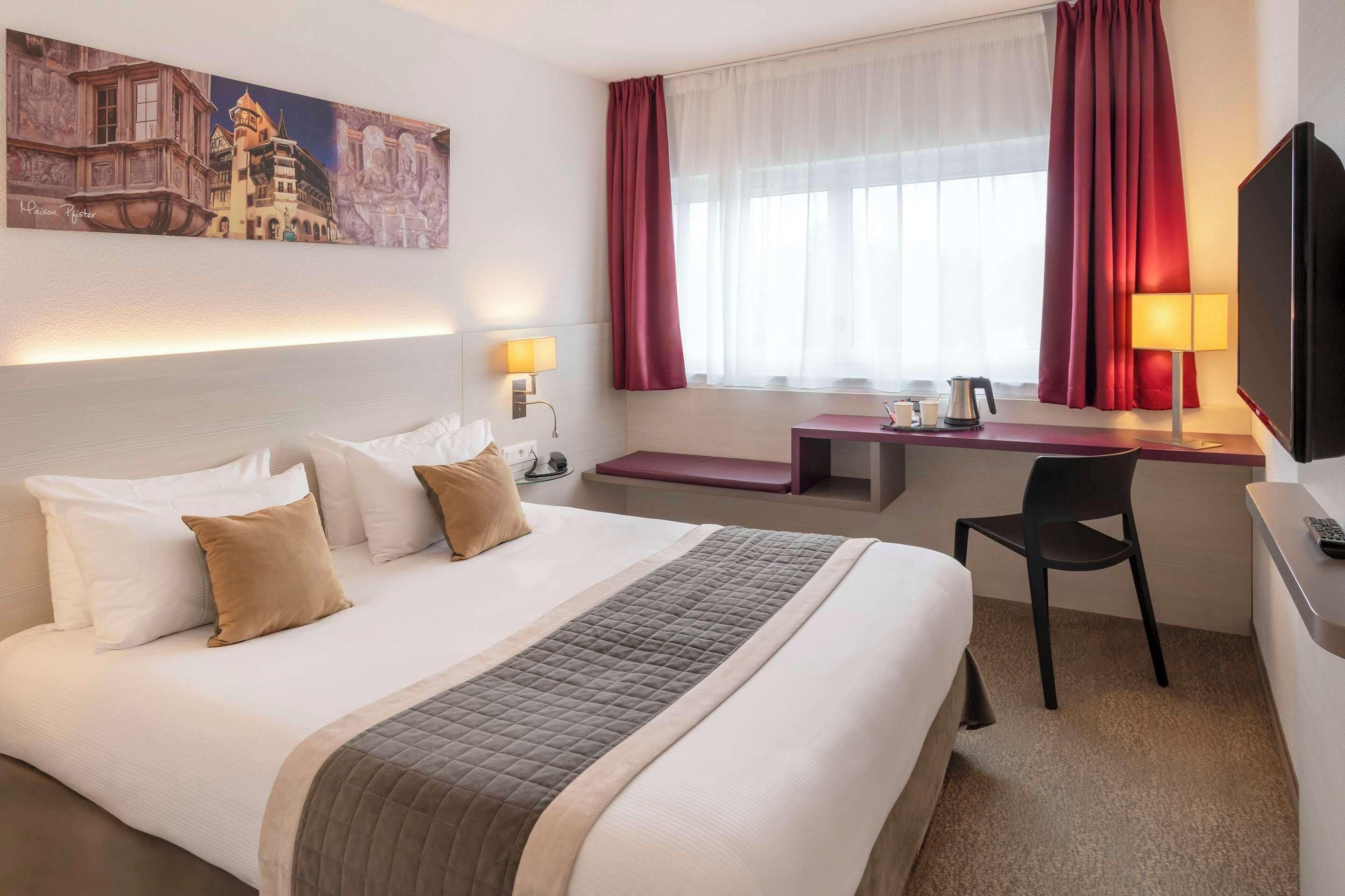 Een hotelkamer met een groot bed, een bureau, een stoel, een televisie en een schilderij aan de muur.