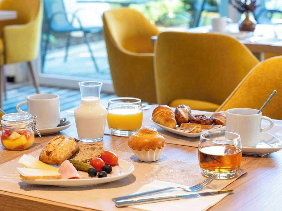 Une table de petit-déjeuner avec divers aliments, un verre de jus d’orange et une tasse de thé.