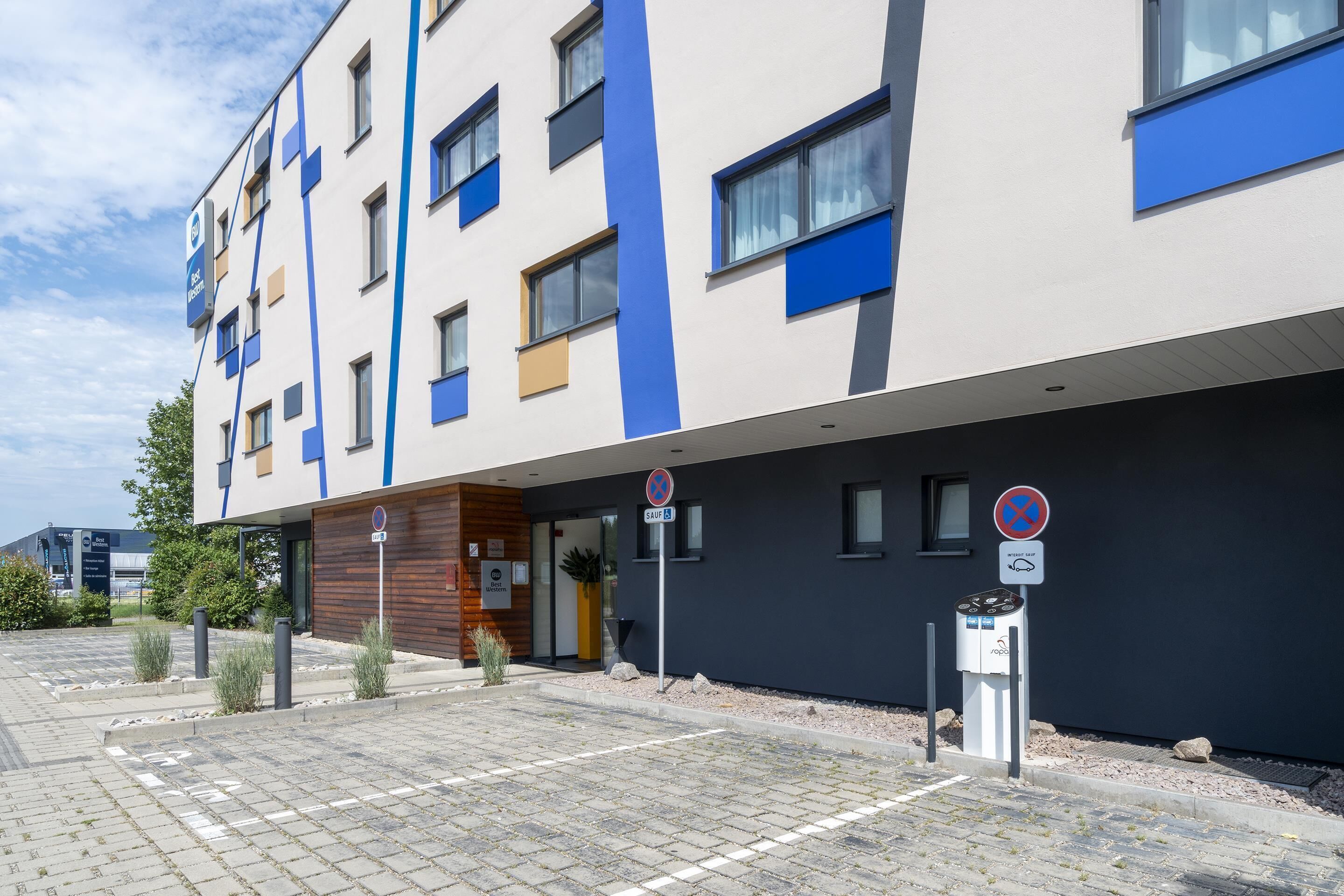 Un bâtiment moderne doté d’un toit plat, de nombreuses fenêtres et d’un espace de stationnement agrémenté d’un panneau indiquant une place réservée aux personnes handicapées.