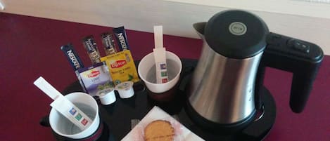 A coffee maker, Lipton tea packets, a muffin, and a cup on a tray.