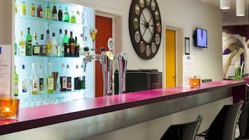 Zona de bar con una variedad de botellas de licores, un dardo y un reloj en la pared.