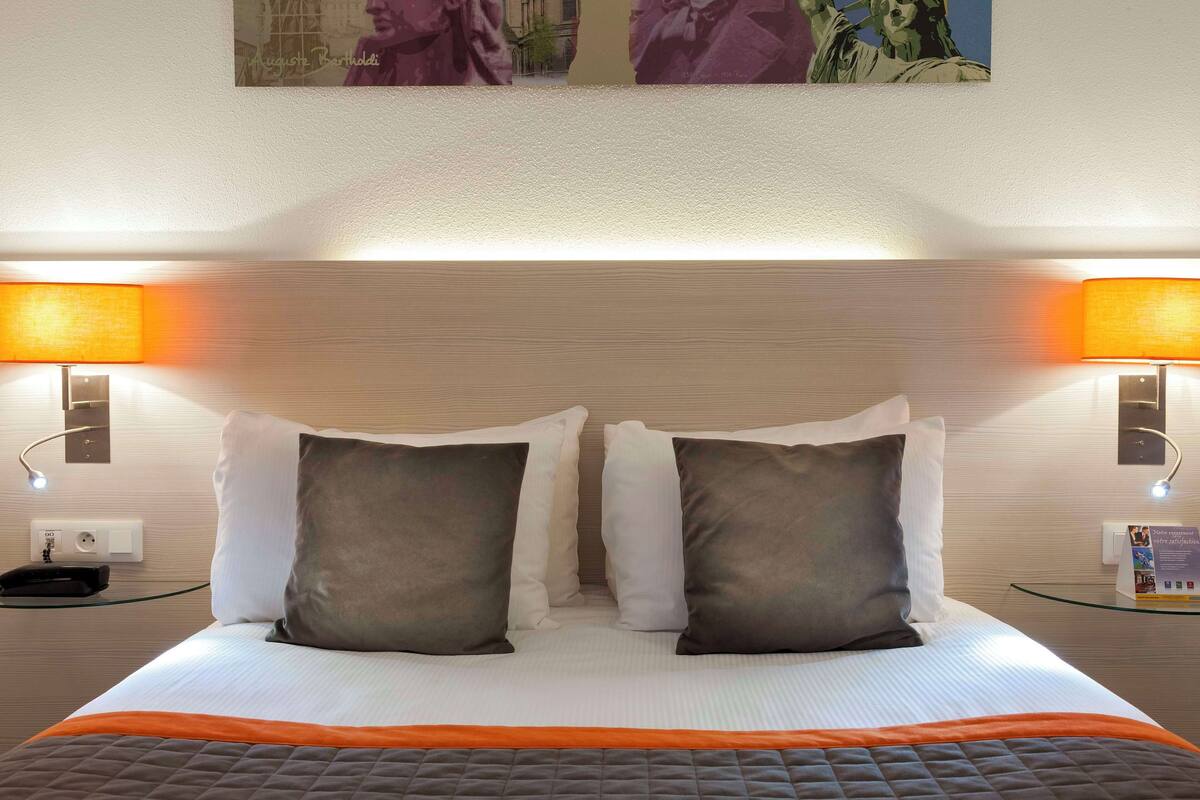 Quarto de hotel com cama bem arrumada, duas luminárias de cabeceira e um quadro sobre a cama.