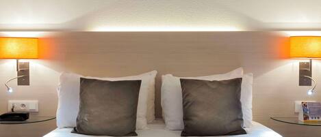 A hotel room with a neatly made bed, two bedside lamps, and a painting above the bed.
