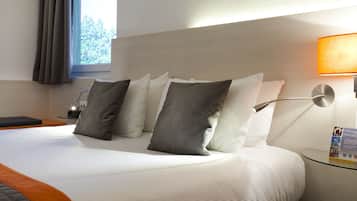 Une chambre d’hôtel avec un lit bien fait, une table de chevet avec une lampe et une fenêtre avec des rideaux.