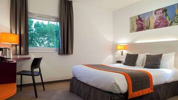 A hotel room with a bed, a desk, a chair, a window with curtains, and a painting on the wall.