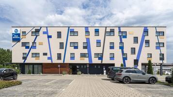 Een modern gebouw met een geometrisch gevelontwerp, een parkeerplaats en een heldere lucht.