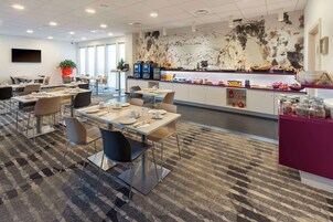 Un comedor moderno de hotel con mesas, sillas, una barra de cocina y un mural grande en la pared.