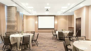 A conference room with round tables and chairs, a projector screen, and a carpeted floor.
