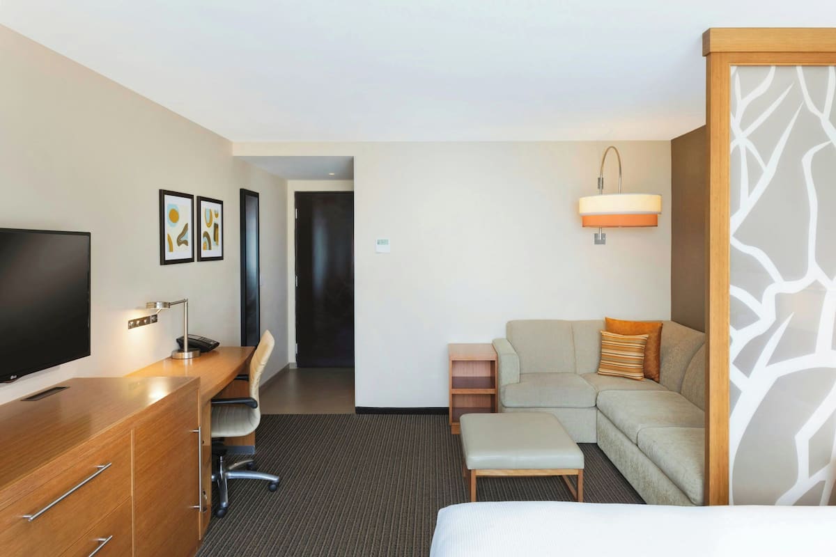 A hotel room with a wooden desk, a television, a sofa, and a bed.