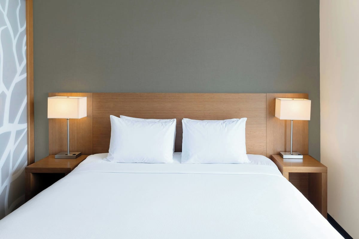 A hotel room with a large bed, two bedside tables with lamps, and a plain wall.
