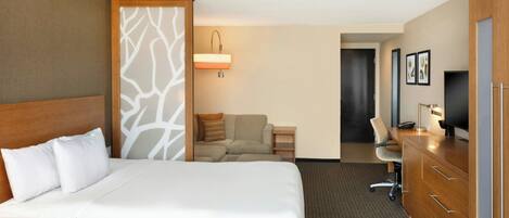 Ett hotellrum med en stor säng, ett skrivbord, en stol, en tv och en garderob.