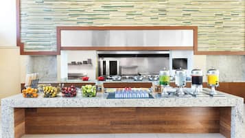 A modern kitchen with a granite countertop, a stainless steel range hood, and a variety of food items and drink dispensers.