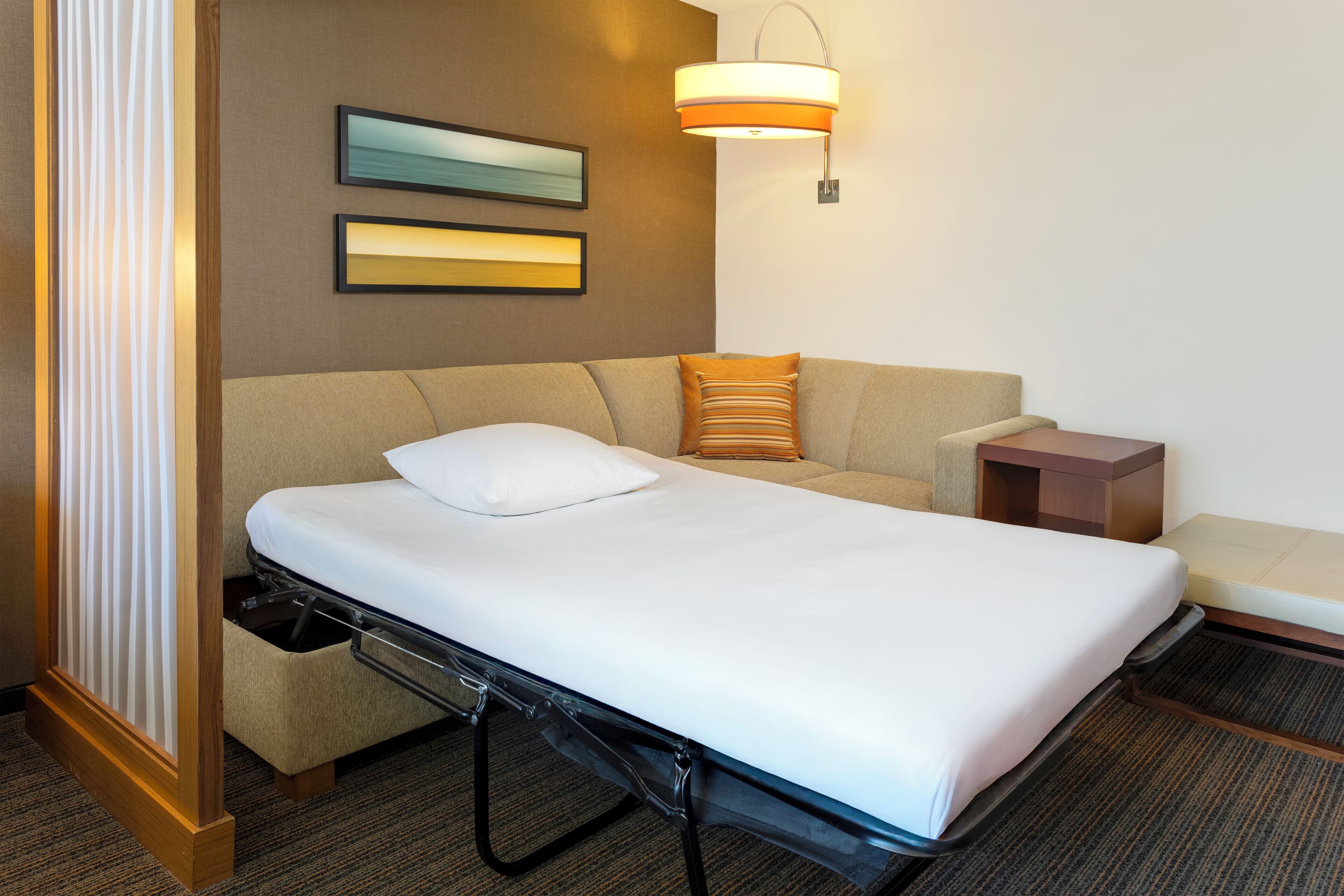 Een hotelkamer met een bed, een sofa, een nachtkastje, een lamp en twee ingelijste foto’s aan de muur.