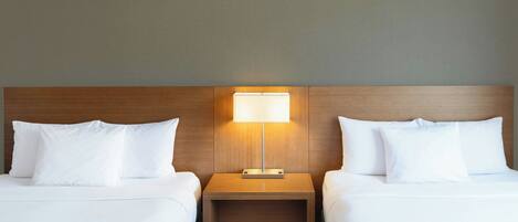 A hotel room with two beds, a nightstand with a lamp, and a wooden headboard.