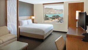 Habitación de hotel con cama, escritorio, silla y un amplio ventanal con vistas al mar y las colinas.