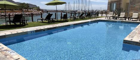 A pool area with clear blue water, lounge chairs, and umbrellas.