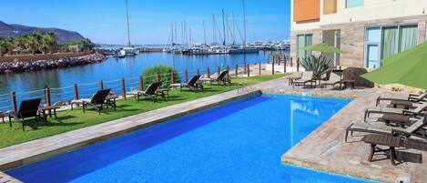 A swimming pool with lounge chairs and a view of boats in the background.