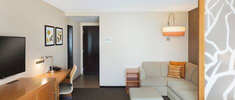 Una habitación de hotel con una cama, un escritorio con televisor, un sofá y una mesita.