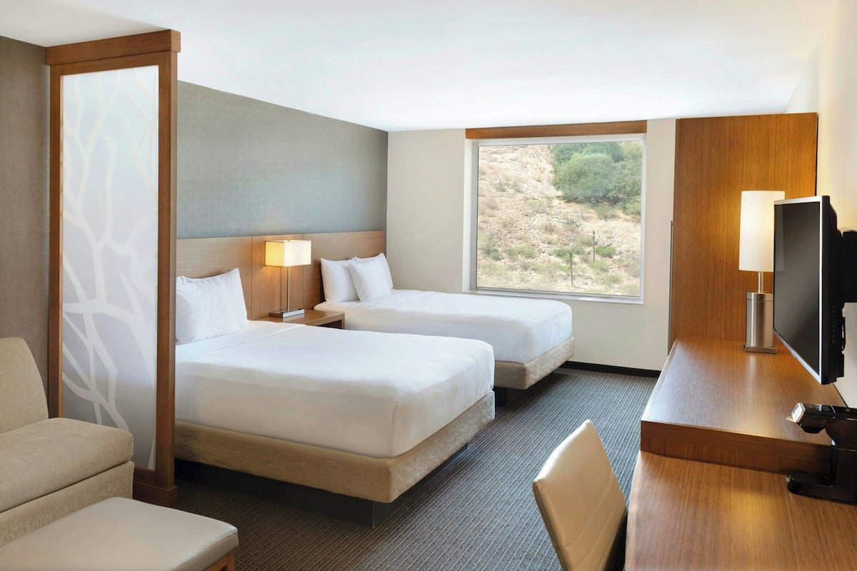 A hotel room with two beds, a desk with a TV, and a window with a view of the outdoors.