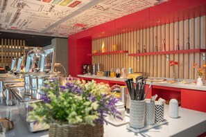 Zona de bufé con diferentes estaciones de comida, un arreglo floral central y una decoración en tonos rojo y beige.