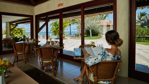 A woman seated at a table with a laptop, overlooking a patio with outdoor seating and a view of the ocean. - Gungaporanga Hotel (Barra de São Miguel)