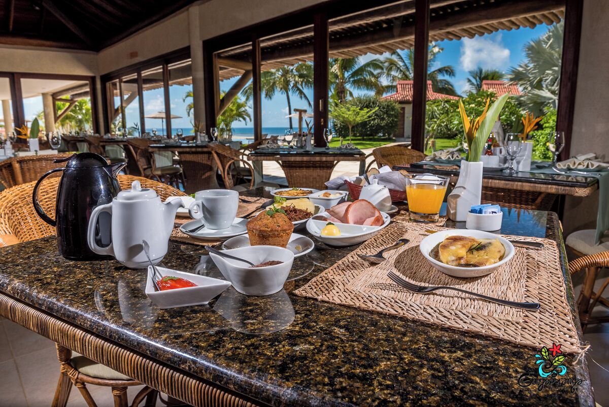 A breakfast table with various dishes, a coffee pot, and a view of the ocean.