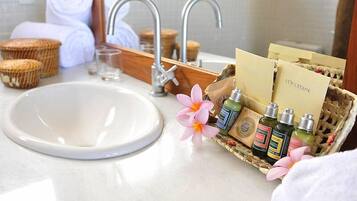A bathroom with a white sink, two faucets, a mirror, and a wicker basket containing toiletries and a card.