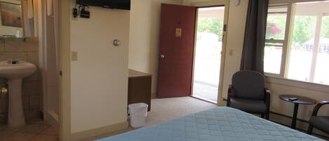 A hotel room with a bed, a sink, a mirror, a television, a door, and a window.